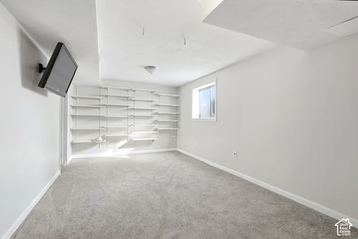 Wall-mounted shelving system, recessed window, wall-mounted television bracket, neutral carpet flooring, and flush-mount ceiling light fixture