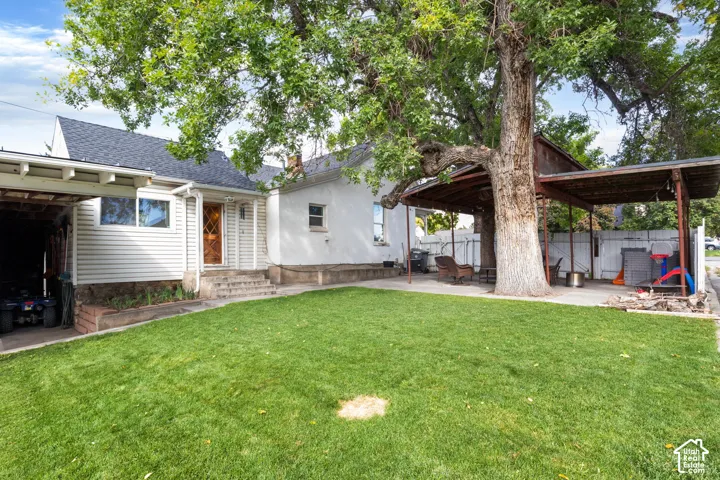 Expansive green lawn with a mature shade tree, concrete patio, and covered outdoor area