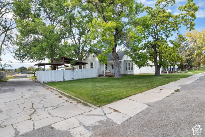 White painted exterior with a bay window, mature trees, and a spacious lawn