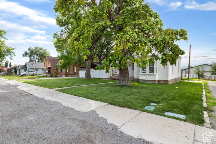 Manicured front lawn with mature trees, a defined concrete sidewalk, and a white picket fence