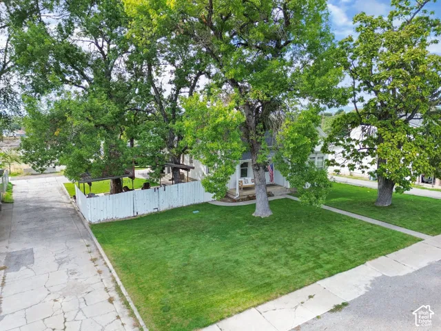 Expansive green lawn, mature shade trees, white picket fence, covered patio structure, and a concrete driveway