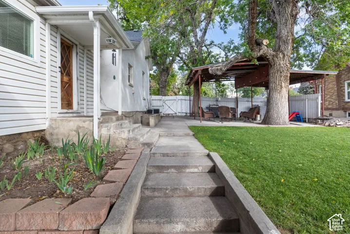 Manicured lawn with mature trees, concrete pathway, and covered patio structure