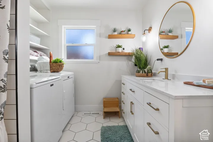 White hexagonal tile flooring, double vanity with white cabinetry, gold-finish hardware, and a white countertop