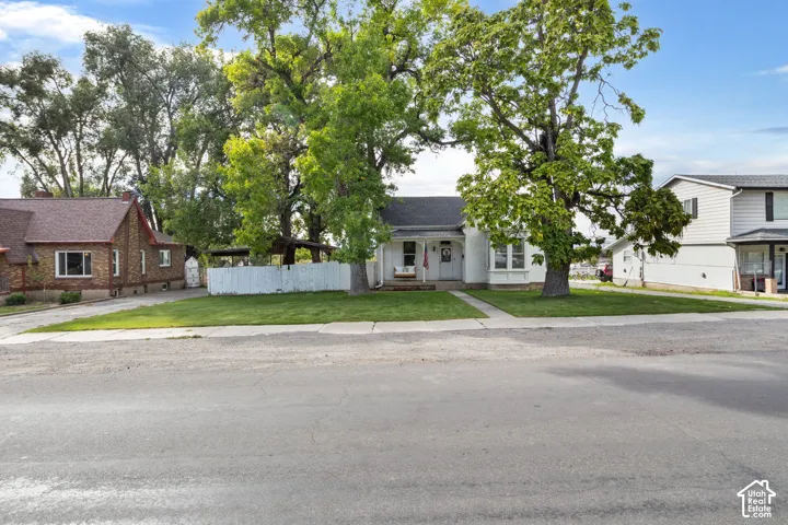 White exterior with an inviting front porch, mature trees, and a well-maintained lawn