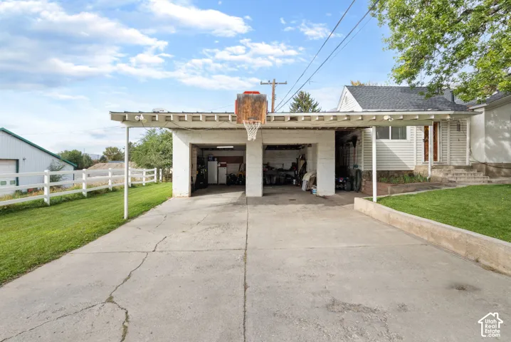 Detached carport with integrated garage bays, concrete driveway, and white picket fencing