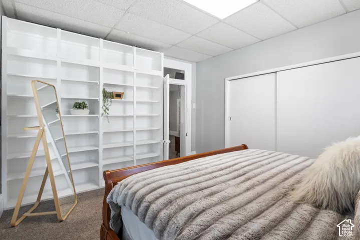 Recessed lighting and ceiling tiles illuminate the room, featuring a wall of built-in white shelving, white sliding closet doors, and light gray wall paint