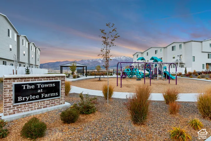 Community sign featuring brickwork, a playground with swings and slides, a covered gazebo, and townhome-style residences