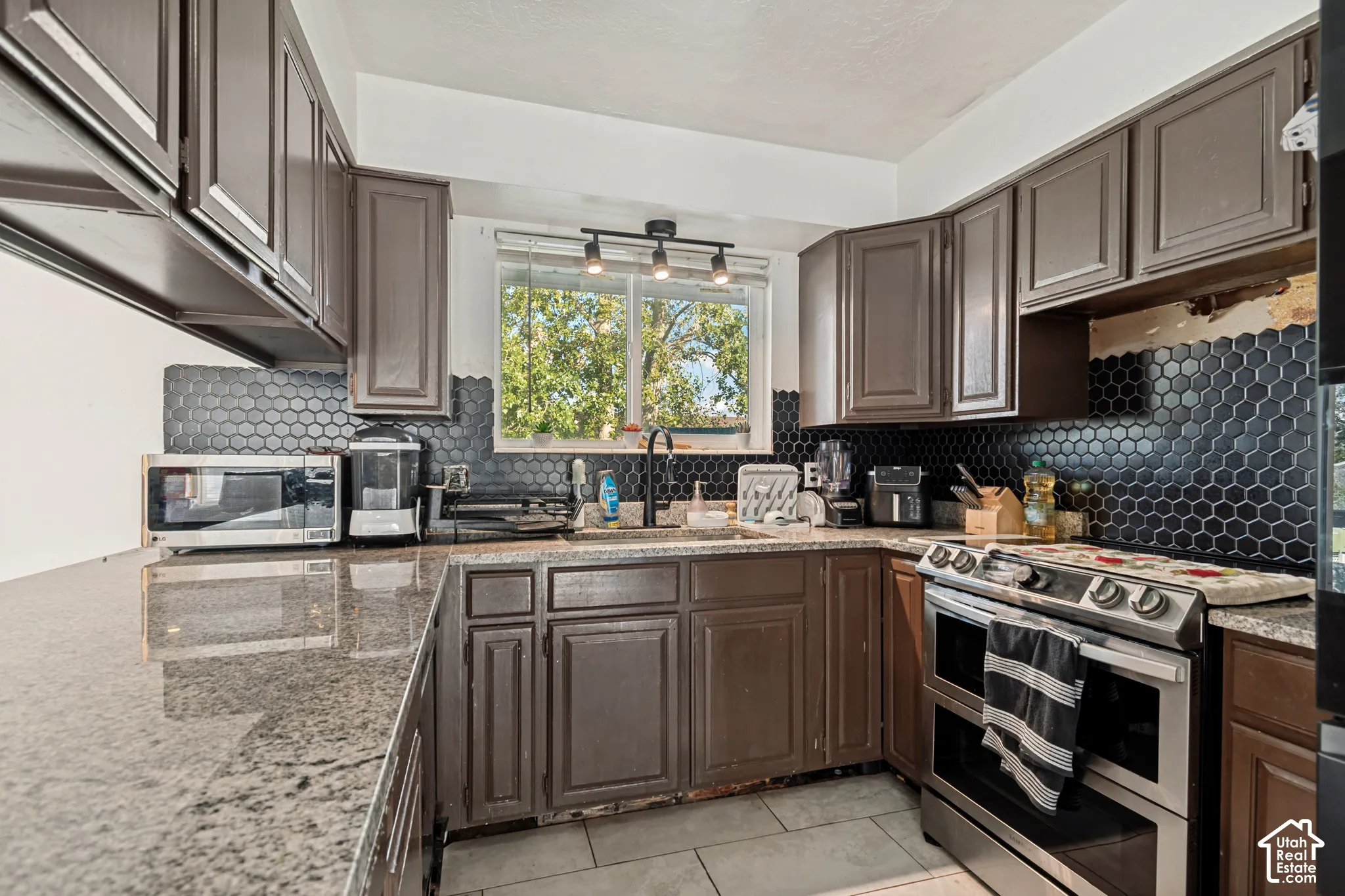 Kitchen featuring dark cabinetry, dark hexagonal tile backsplash, light-toned countertops, stainless steel range, and tile flooring