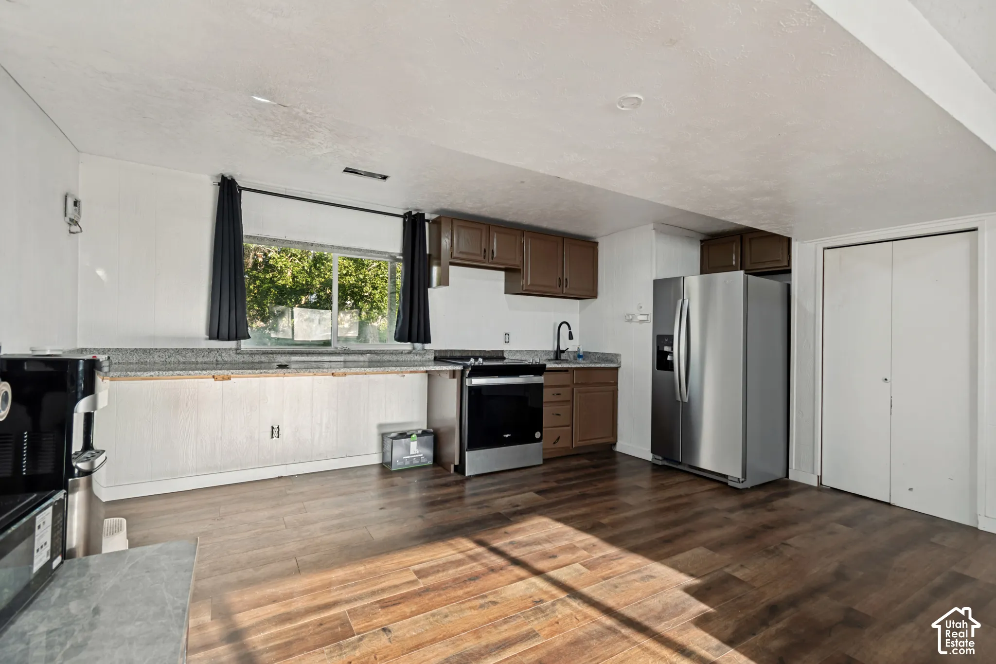 Kitchen featuring wood-finish flooring, dark wood cabinetry, granite countertops, and stainless steel appliances