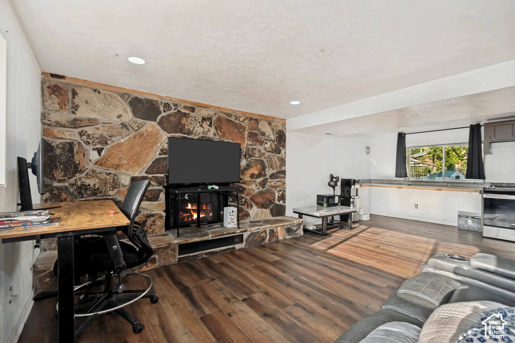 Stone accent wall with a built-in fireplace, wood-finish flooring, recessed lighting, and a built-in kitchen counter with a window