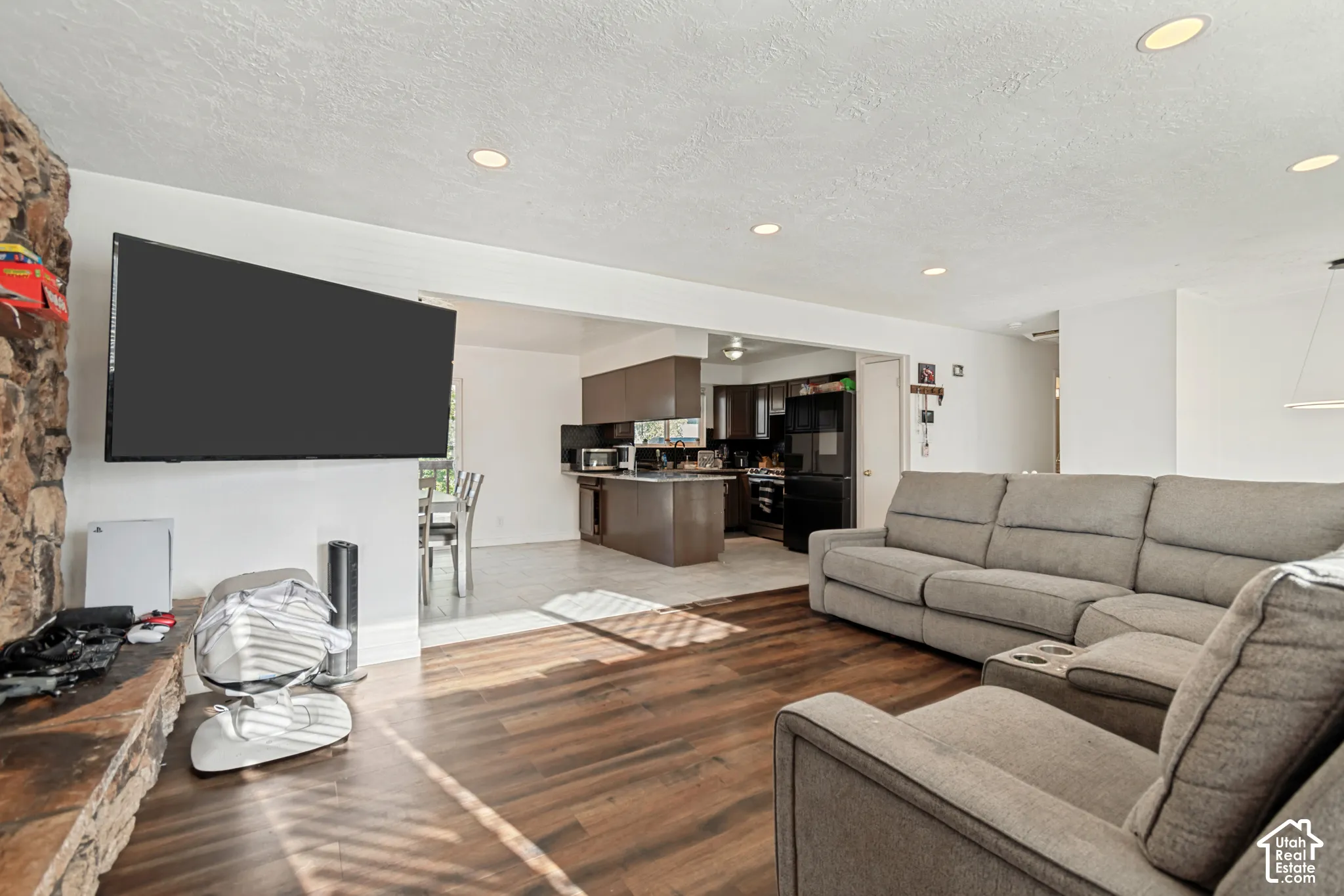 Open-concept living area with wood-finish flooring, recessed lighting, and a stone-clad fireplace