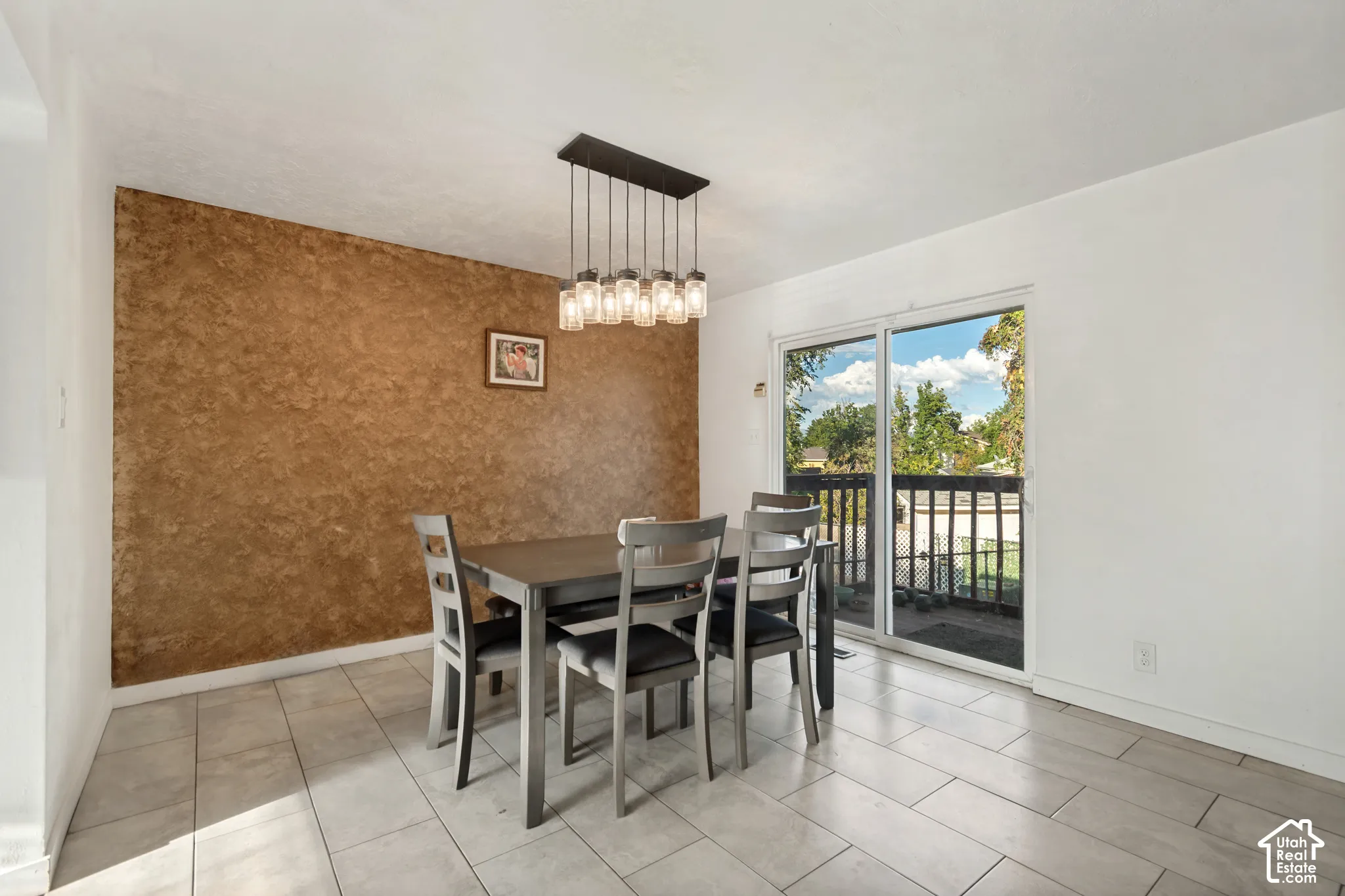 Tile flooring, textured accent wall, sliding glass door, and a linear chandelier with multiple glass shades