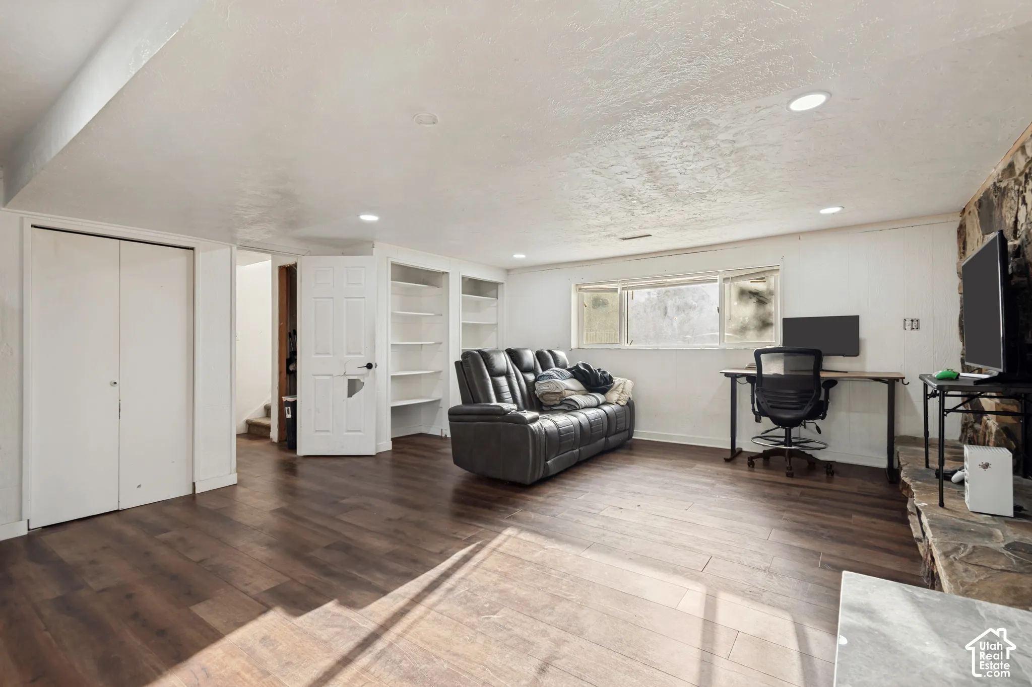 Wood-finish flooring, recessed lighting, built-in shelving, stone-finish accent wall, and a horizontal window