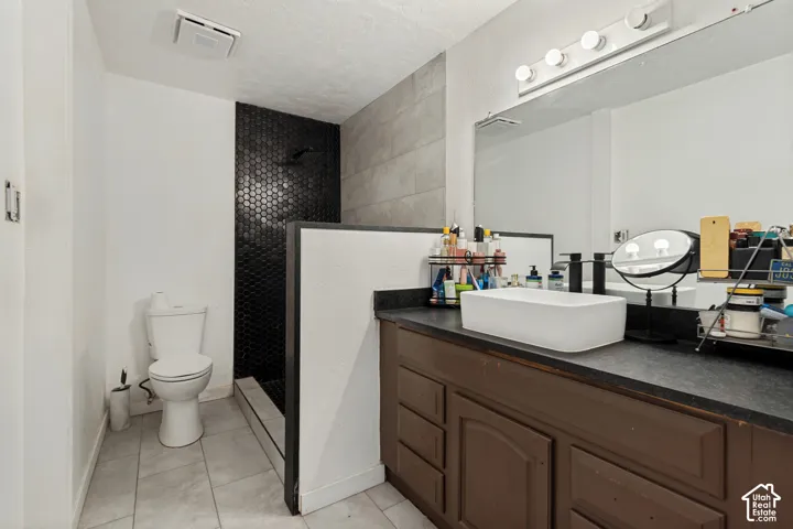 Tiled flooring with a hexagon-tiled shower wall, white rectangular vessel sink, and a mounted vanity light fixture