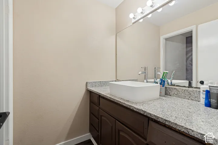 Vanity with a rectangular vessel sink, polished chrome faucet, granite-look countertop, dark wood-finish cabinetry, and a large wall-mounted mirror with integrated lighting