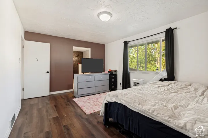 Wood-finish flooring, white door with black hardware, accent wall, window with black curtain rod, and ceiling light fixture