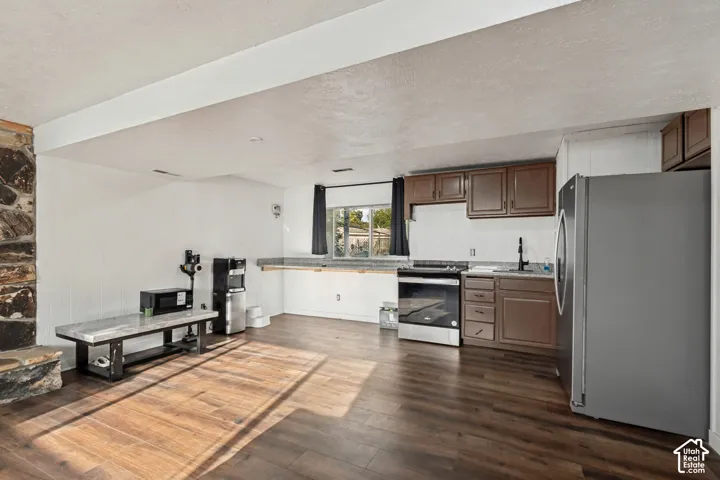 Wood-finish flooring, stone-clad column, kitchen area with brown cabinetry, stainless steel range, and stainless steel refrigerator