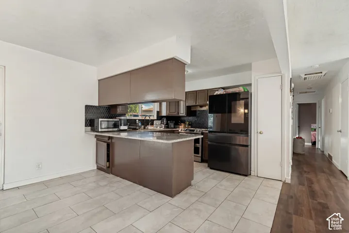 Kitchen featuring a peninsula with a stone-finish countertop, dark brown cabinetry, black tile backsplash, and stainless steel appliances