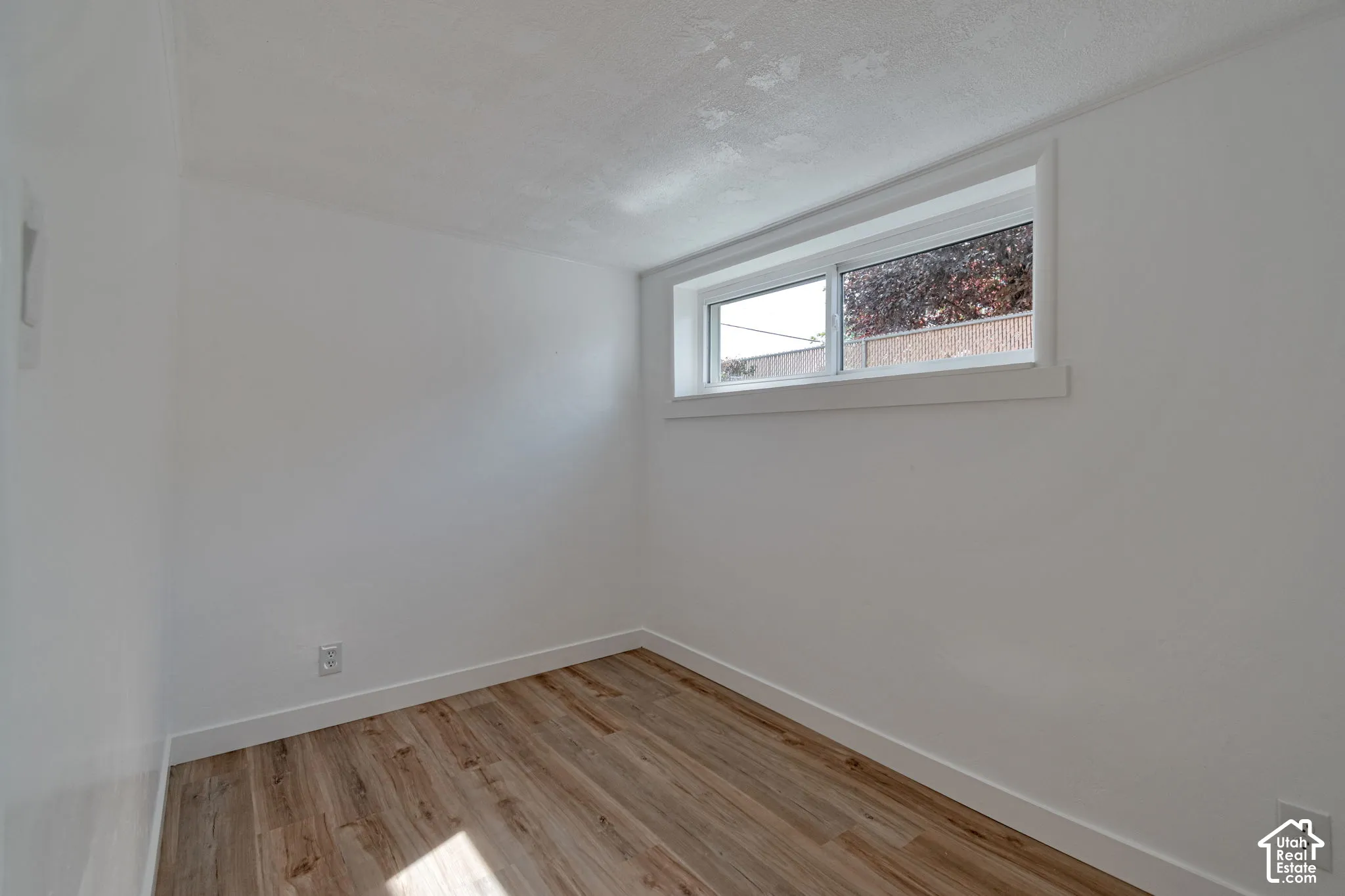 Wood-finish flooring, white walls, and a single window with white trim