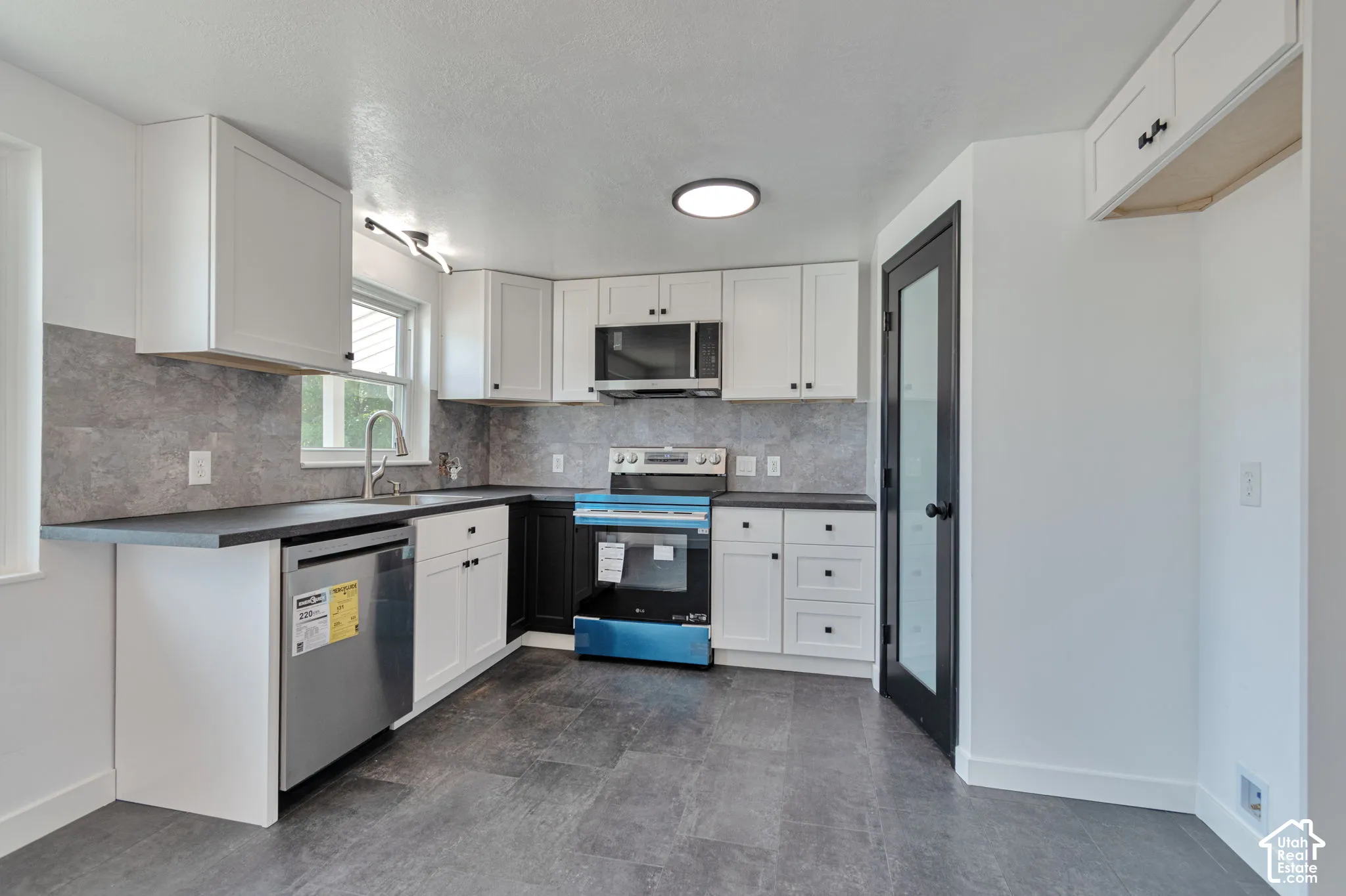 Modern kitchen featuring white shaker cabinetry, dark countertops, a tile backsplash, and stainless steel appliances