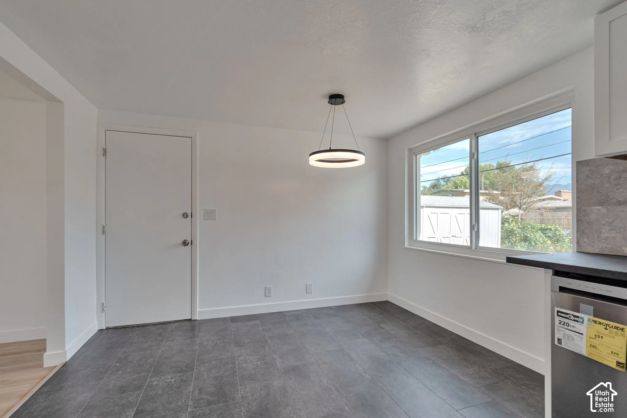 Recessed window, contemporary circular pendant light fixture, dark tile flooring, white baseboards, and a white paneled door