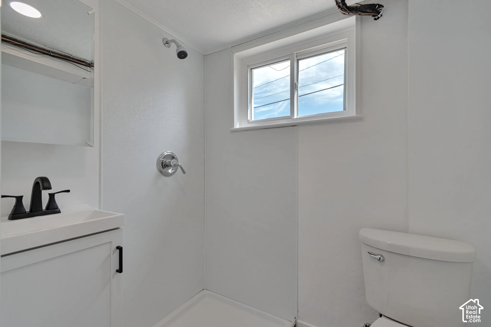 Built-in shower with chrome fixtures, single window, white vanity with black faucet, built-in medicine cabinet, and white toilet