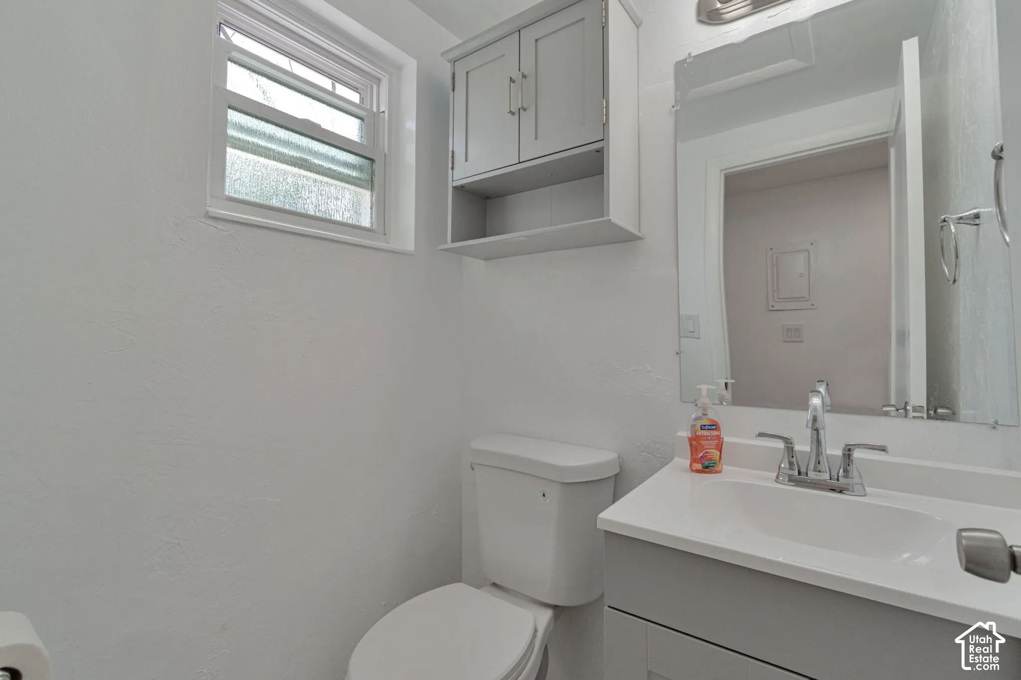 White interior with a built-in toilet, a single-pane window, and a wall-mounted cabinet