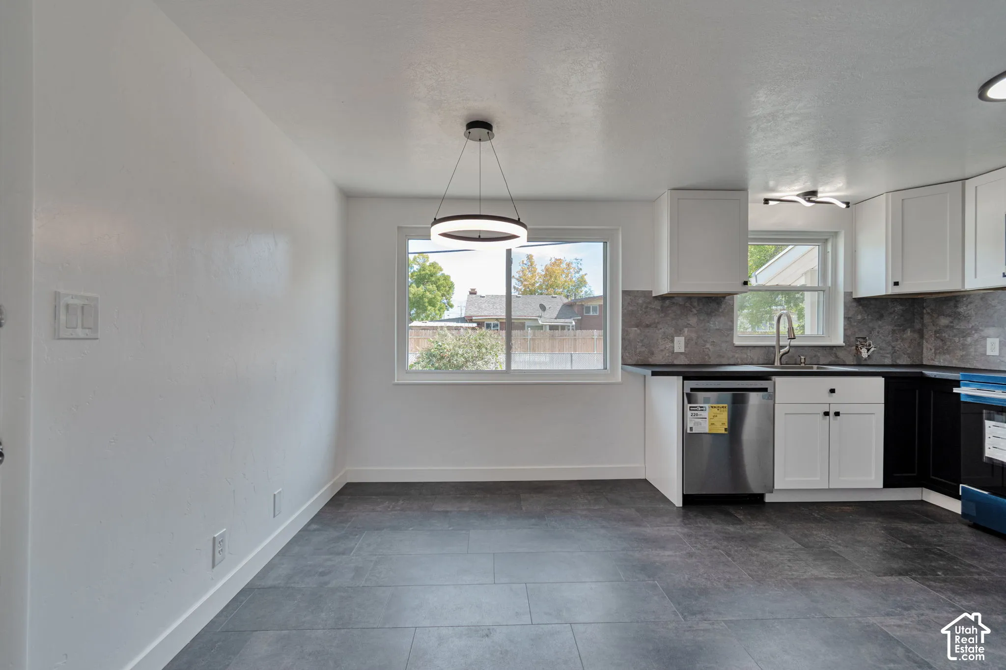 Contemporary kitchen featuring white cabinetry, dark countertops, stainless steel appliances, a tiled backsplash, and dark tile flooring