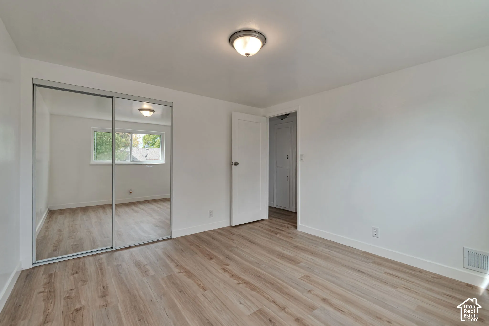 Wood-finish flooring, white walls, mirrored sliding closet doors, and a flush mount ceiling light fixture