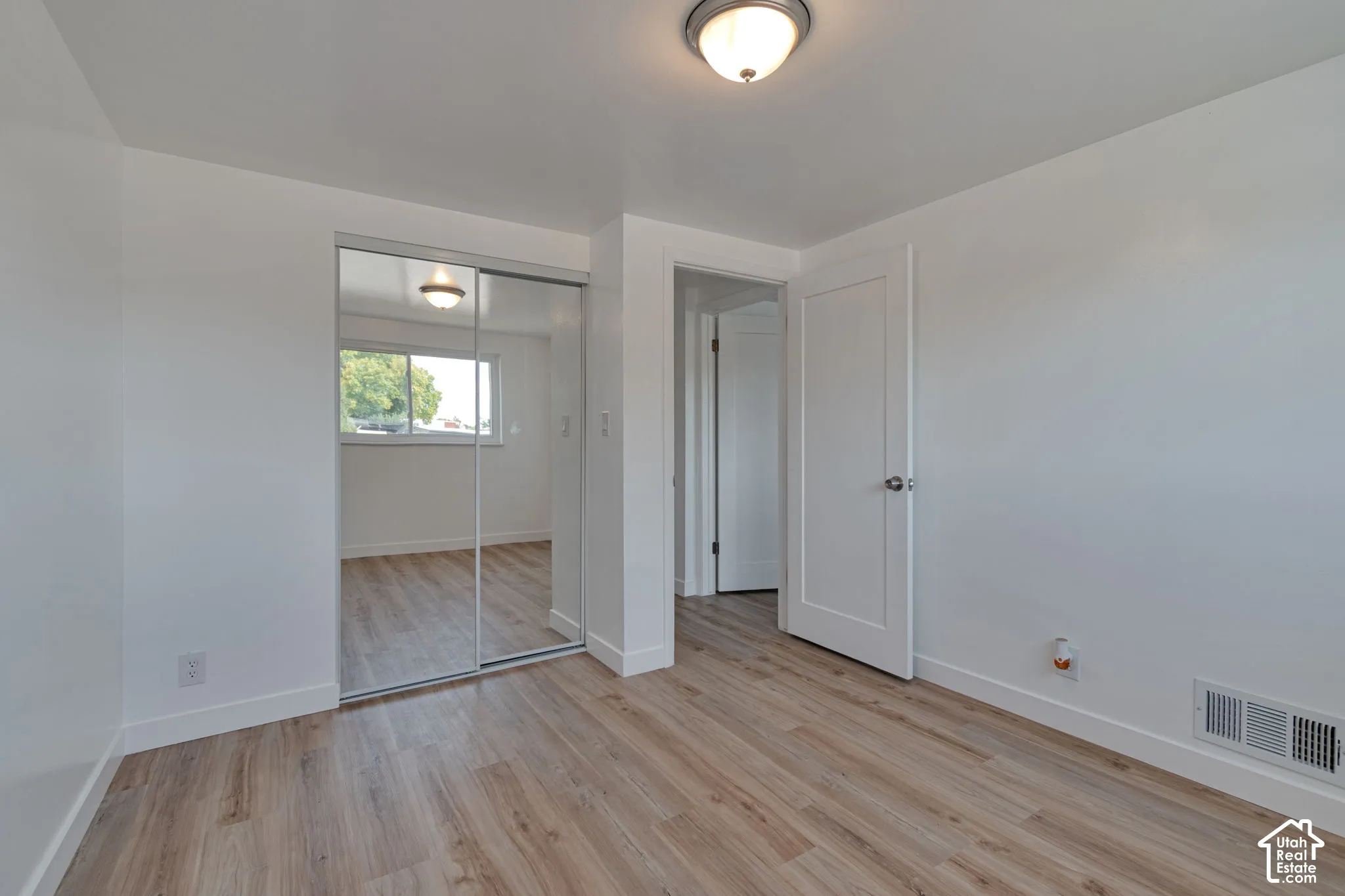 Wood-finish flooring, white walls, white trim, mirrored closet doors, and a flush-mount ceiling light