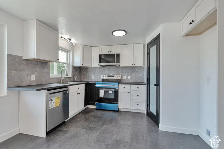Modern kitchen featuring white shaker cabinetry, dark countertops, a tile backsplash, and stainless steel appliances