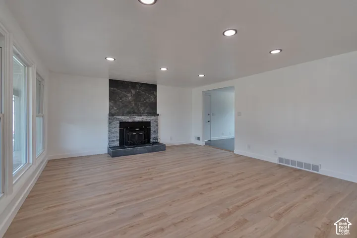 Spacious room featuring wood-finish flooring, recessed lighting, and a fireplace with a stone surround and hearth