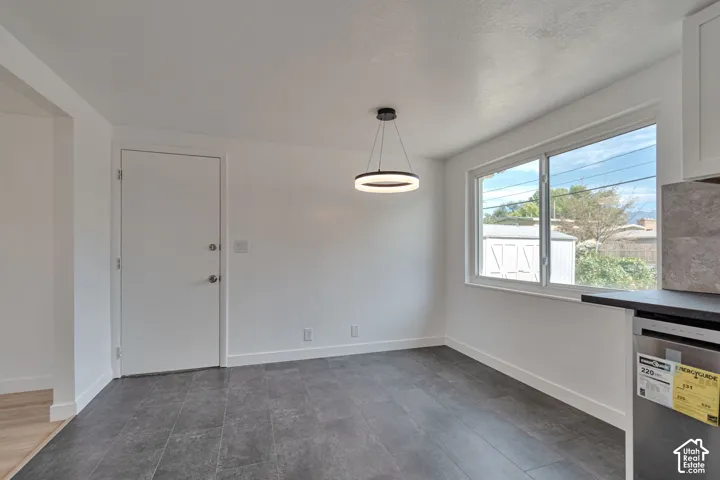 Recessed window, contemporary circular pendant light fixture, dark tile flooring, white baseboards, and a white paneled door