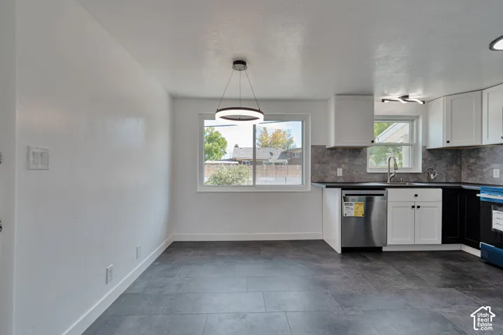 Contemporary kitchen featuring white cabinetry, dark countertops, stainless steel appliances, a tiled backsplash, and dark tile flooring