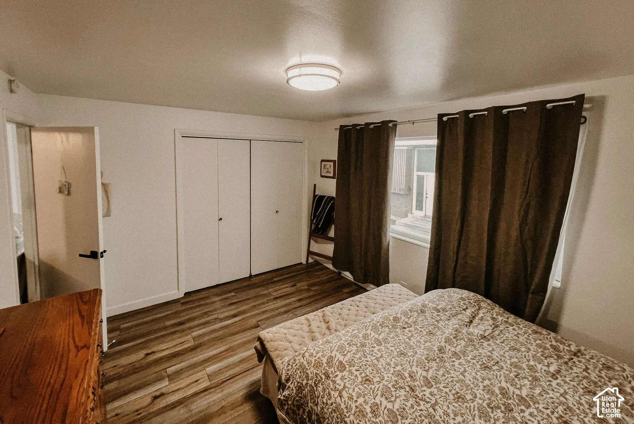 Wood-finish flooring, white walls, double-door closet, window with natural light, and a flush-mount ceiling light fixture