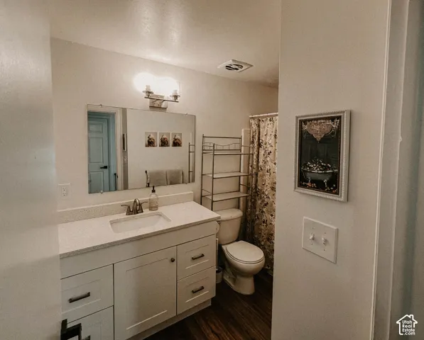 White vanity with a single basin sink, light-toned countertop, wall-mounted mirror, and wood-finish flooring