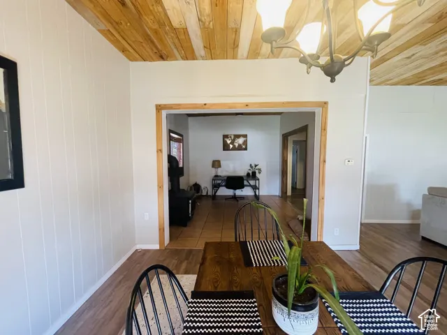 Wood-panel ceiling with a chandelier, vertical white paneling, and an open doorway
