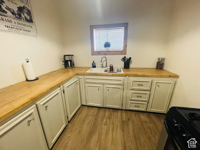 Corner kitchen featuring wood-finish countertops, white cabinetry with silver hardware, a single-basin sink, and wood-finish flooring