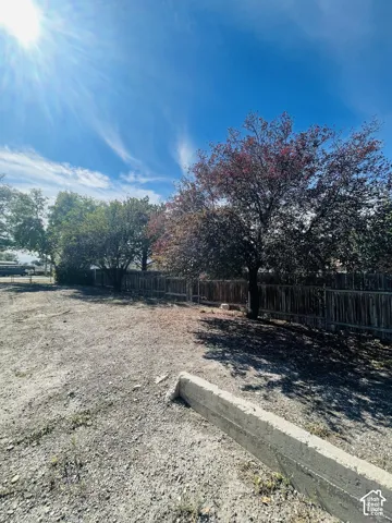 Gravel lot featuring a concrete parking barrier and perimeter fencing