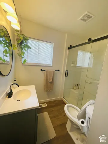 Modern vanity with a white countertop and integrated sink, black-finish faucet, wood-finish flooring, sliding glass shower door, and a window with blinds