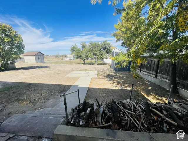 Expansive yard featuring mature trees, a concrete patio, a wooden privacy fence, and two storage sheds