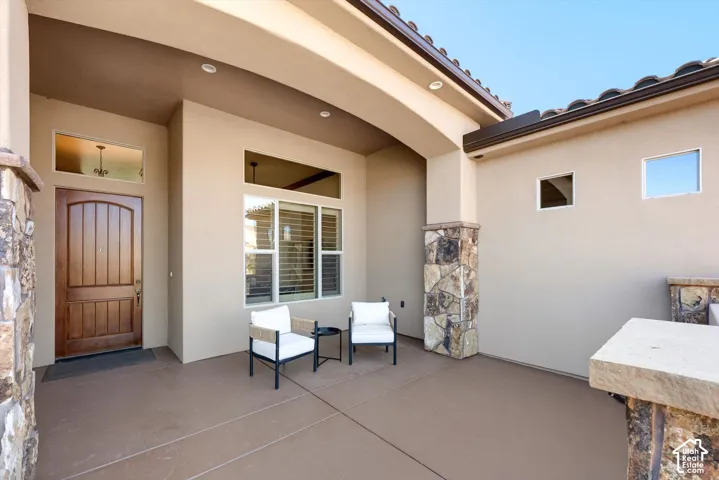 Stucco exterior featuring a wood-panel entry door with transom window, stone-clad columns, and a covered entry porch