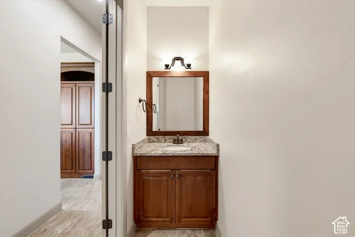 Single vanity with wood-finish cabinetry, stone countertop, undermount sink, and framed mirror