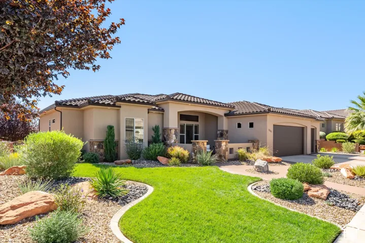 Single-story stucco exterior with a tile roof, stone accents, an integrated two-car garage, and a landscaped front yard with a paved driveway