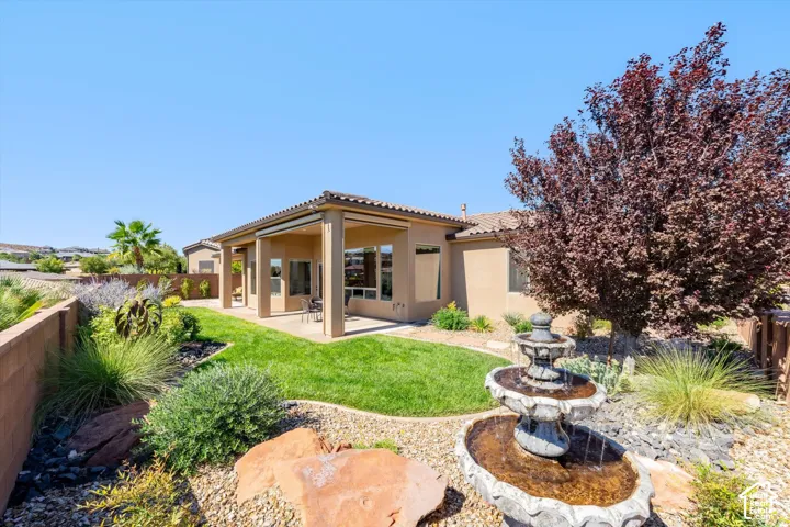 Expansive lawn with a covered patio, tiered fountain, mature landscaping, and privacy wall