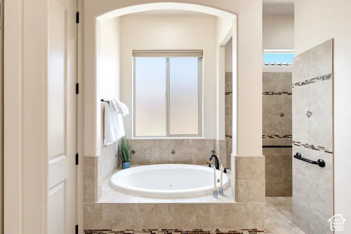 Recessed alcove featuring a built-in soaking tub with a frosted window, surrounded by neutral-toned tile and decorative mosaic accents