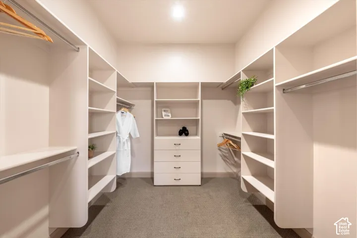Luxurious walk-in closet featuring dual-sided built-in shelving with polished chrome rods, a central dresser with four drawers, recessed lighting throughout, and neutral finishes with textured flooring