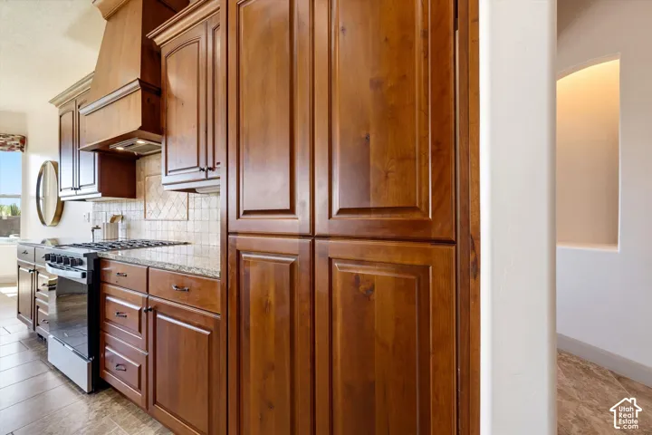 Wood-finish cabinetry, granite countertops, tile flooring, tile backsplash, and a built-in range hood