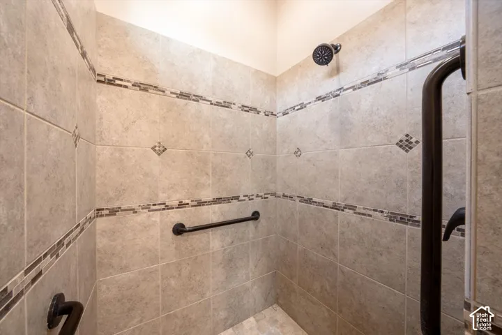 Tiled shower with decorative accent bands, multiple grab bars, and a dark bronze shower fixture