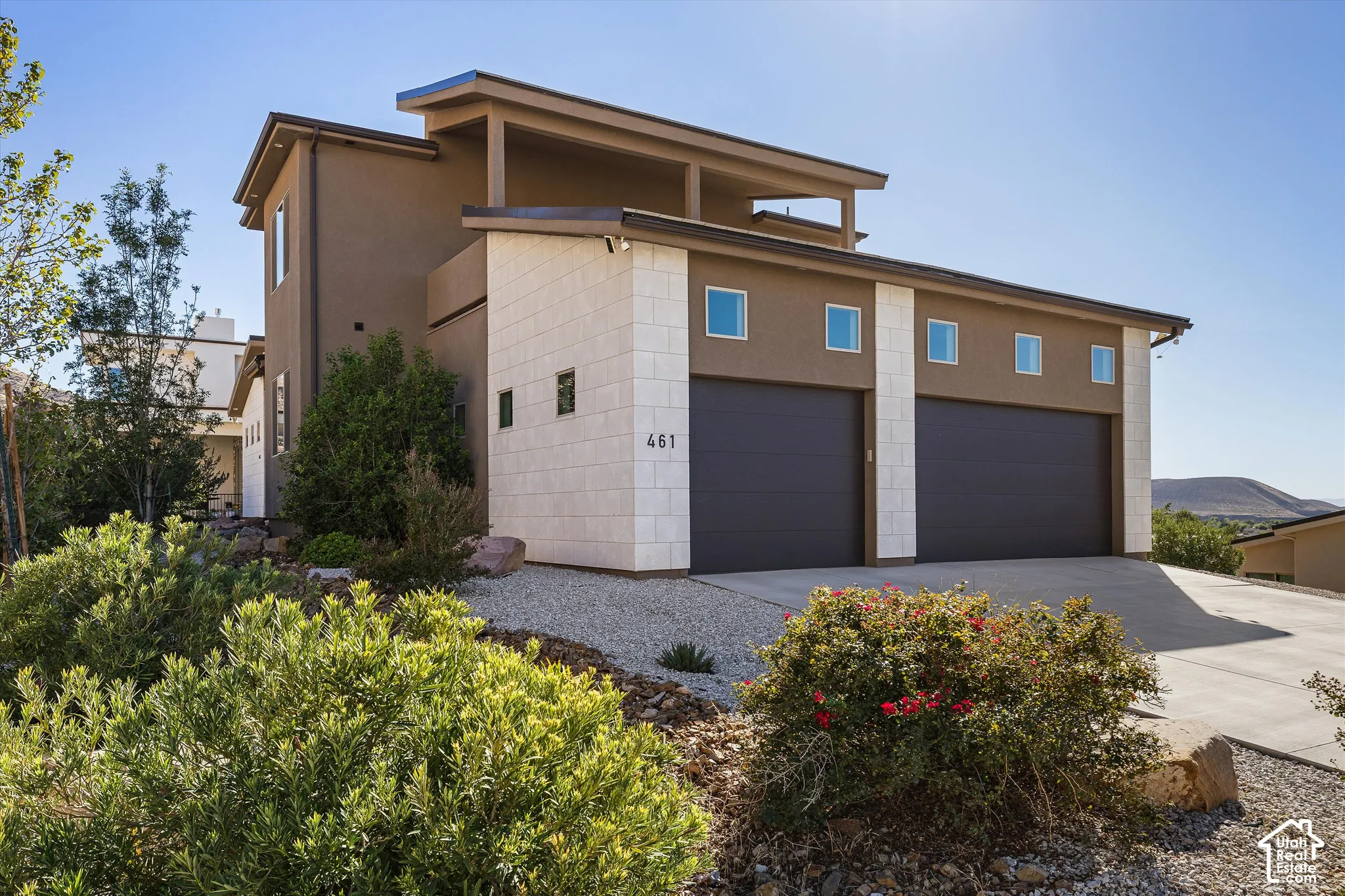 Contemporary exterior with stucco and stone accents, two dark garage doors, and a concrete driveway